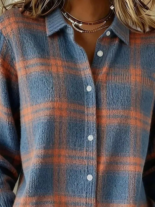 A close-up of a person wearing a textured, long-sleeve button-up shirt with a blue and orange plaid pattern. The shirt features white buttons and is styled with layered silver necklaces.