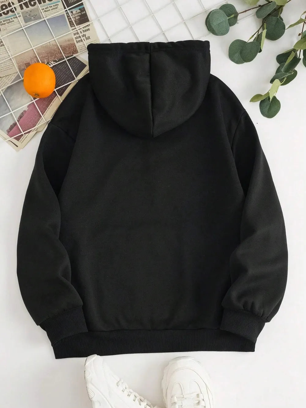 Black hoodie on a white surface with an orange and green leaves in the background