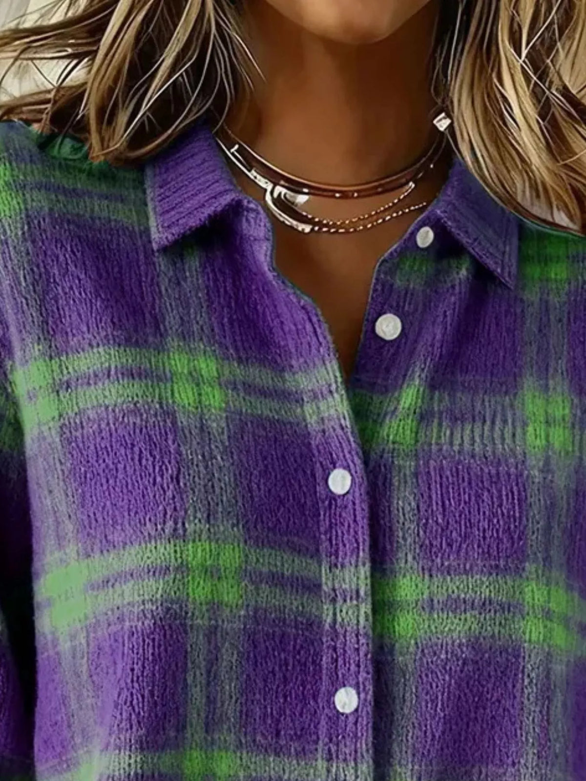 Close-up of a person wearing a fuzzy knit button-up shirt with a purple and green plaid pattern, layered with multiple silver necklaces.