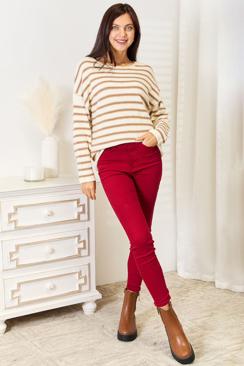 Woman wearing a striped sweater and red pants standing in a room with white furniture.