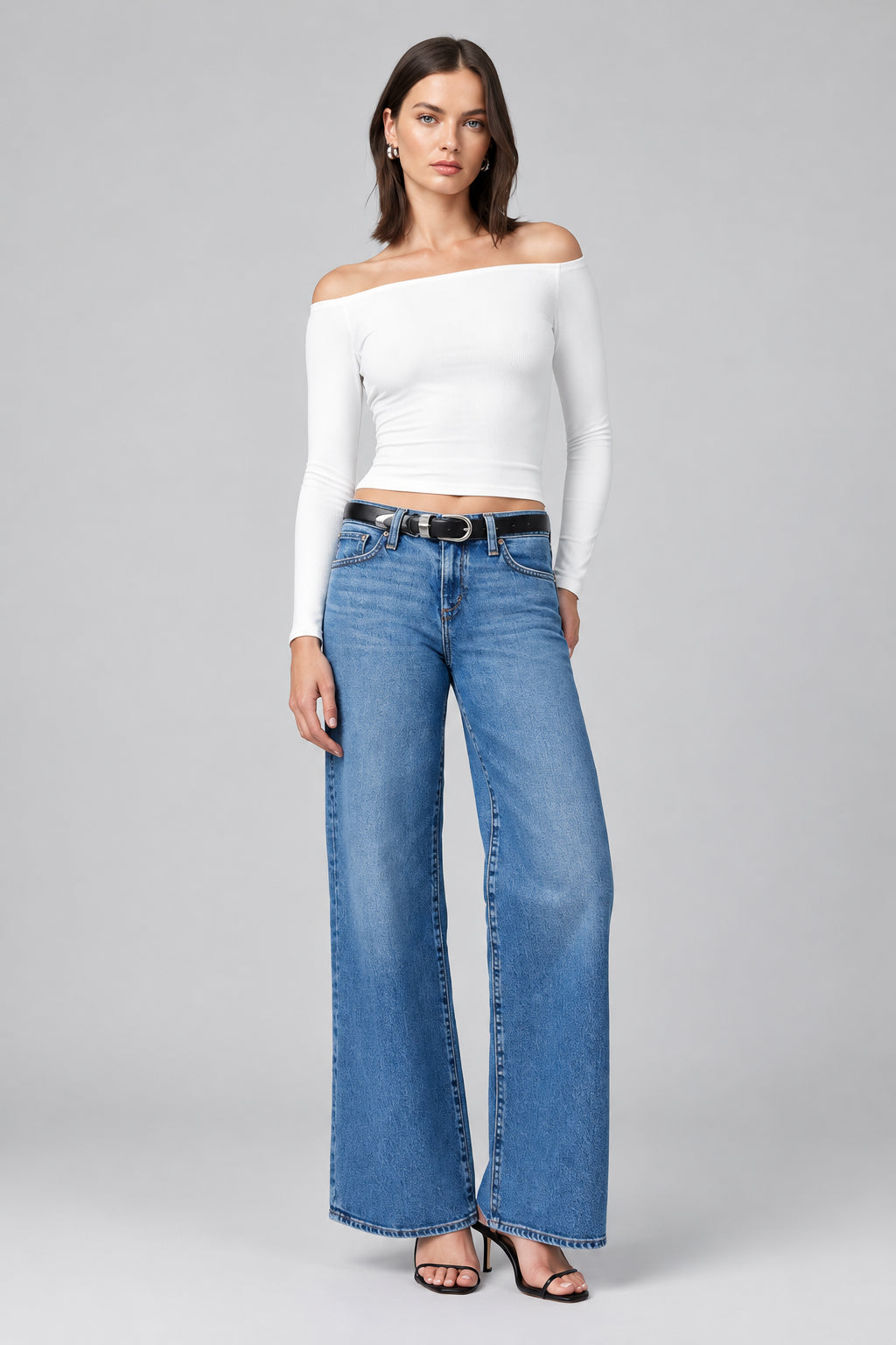Woman wearing a white off-shoulder top and blue jeans on a plain background