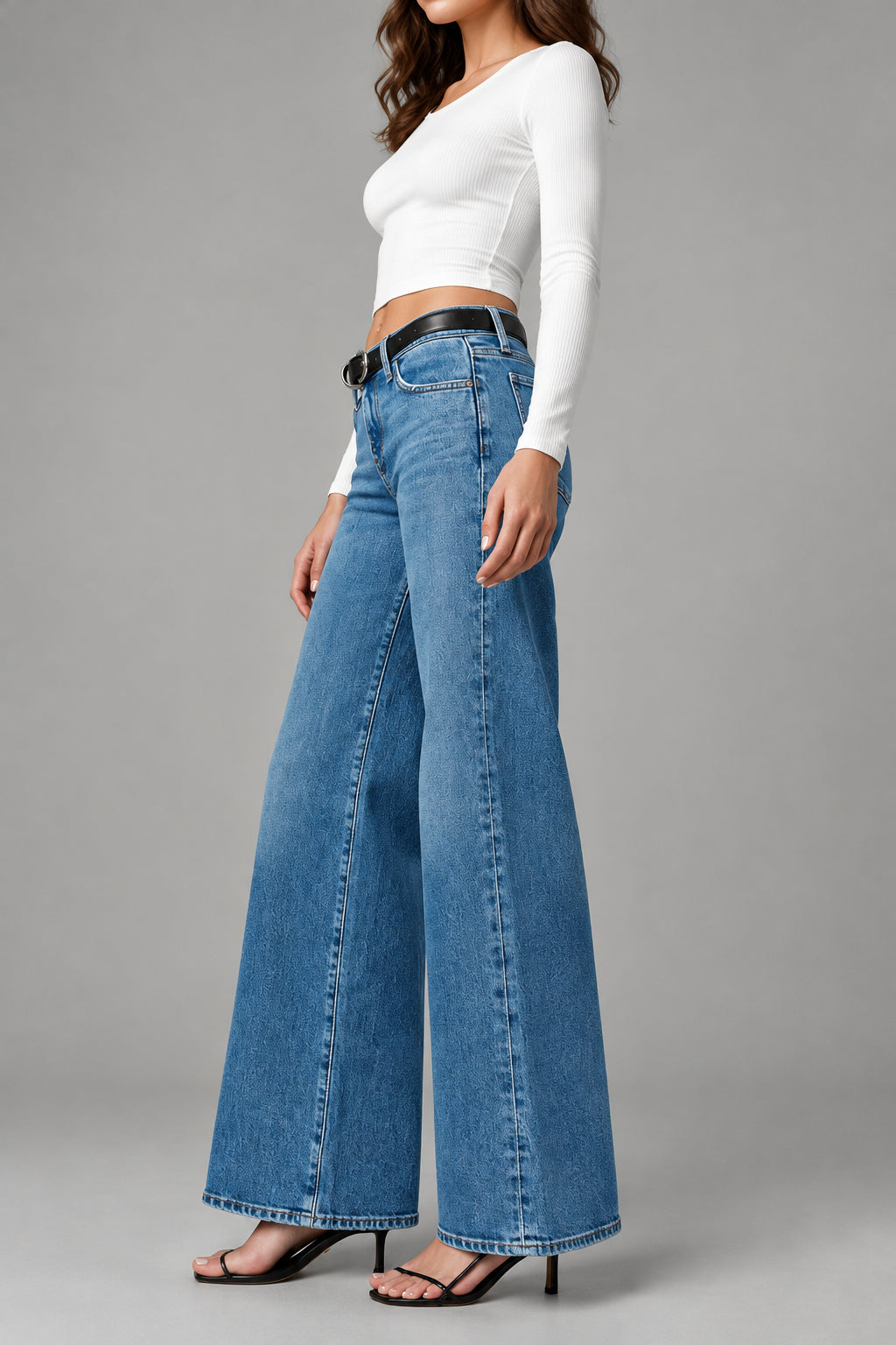 Person wearing blue jeans and a white top on a plain background