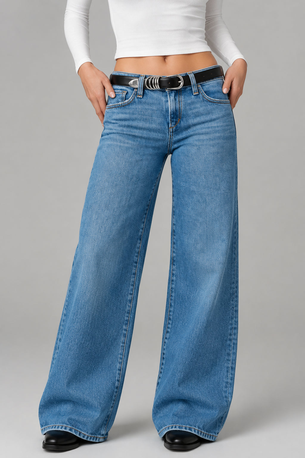 Person wearing blue jeans with a black belt on a plain background