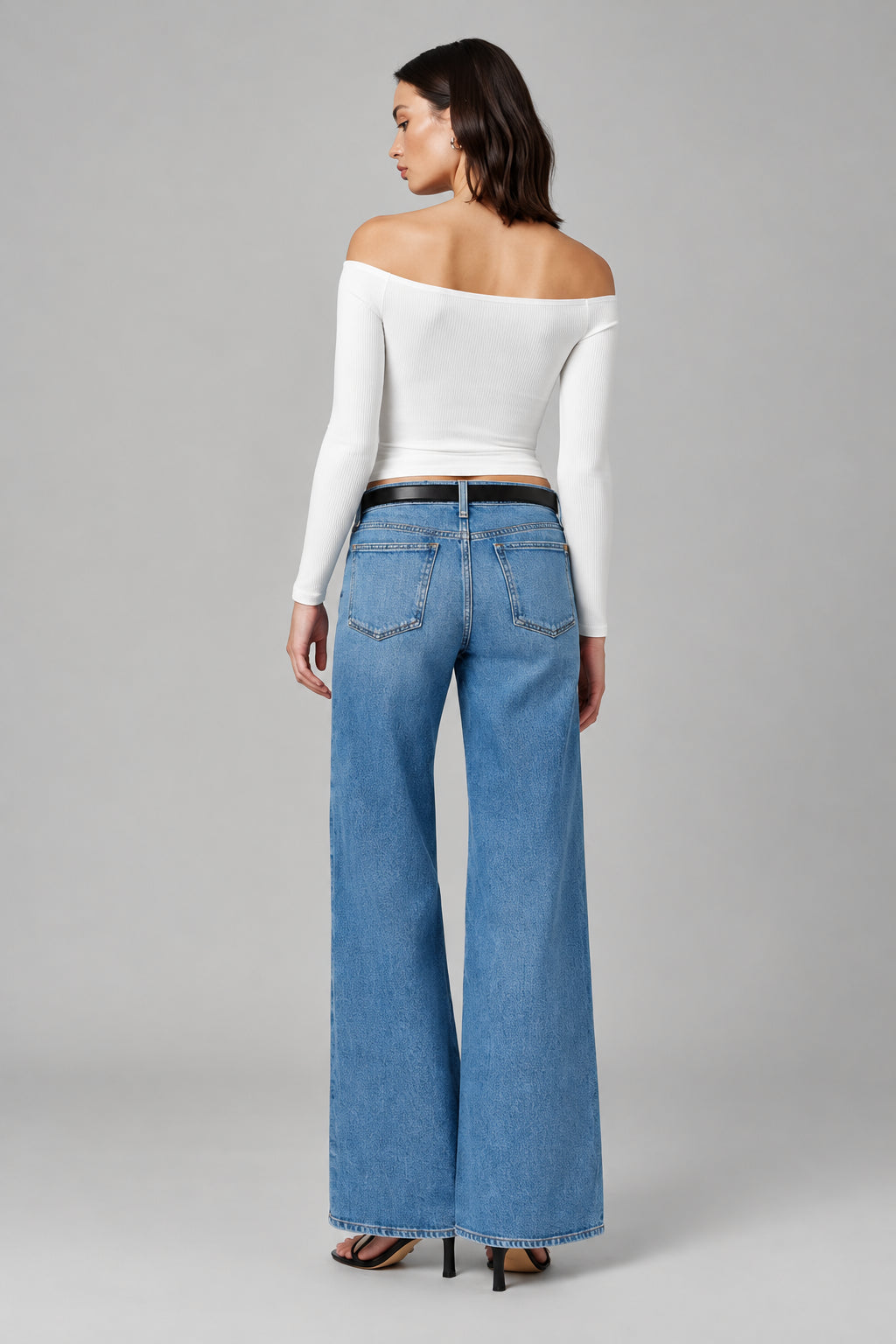 Woman wearing a white off-shoulder top and blue jeans on a plain background