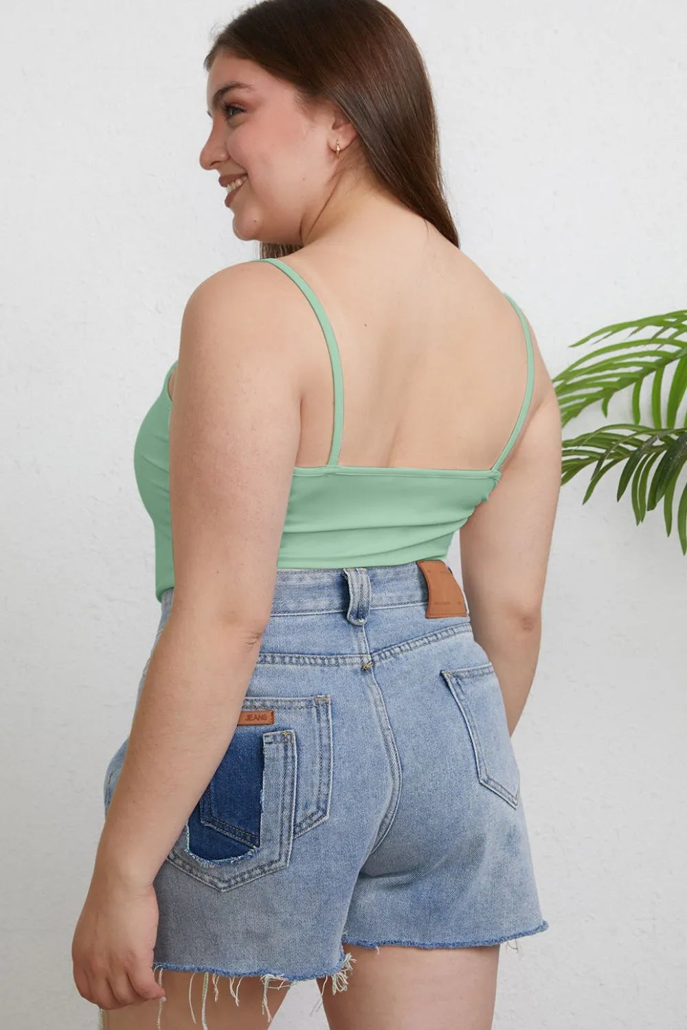 Woman wearing a green top and denim shorts against a white background