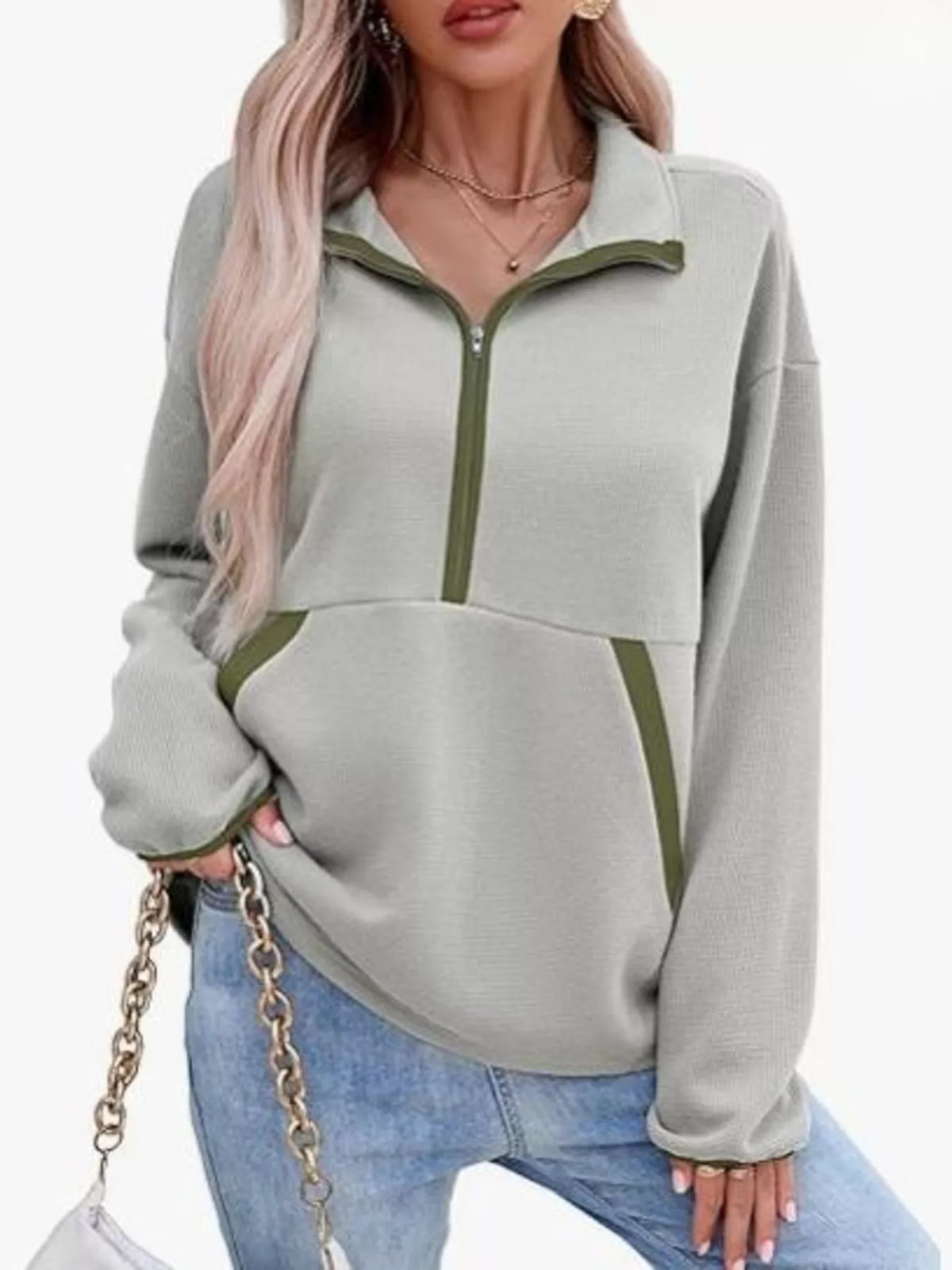 Person wearing a gray and green pullover with a zipper, standing against a white background.
