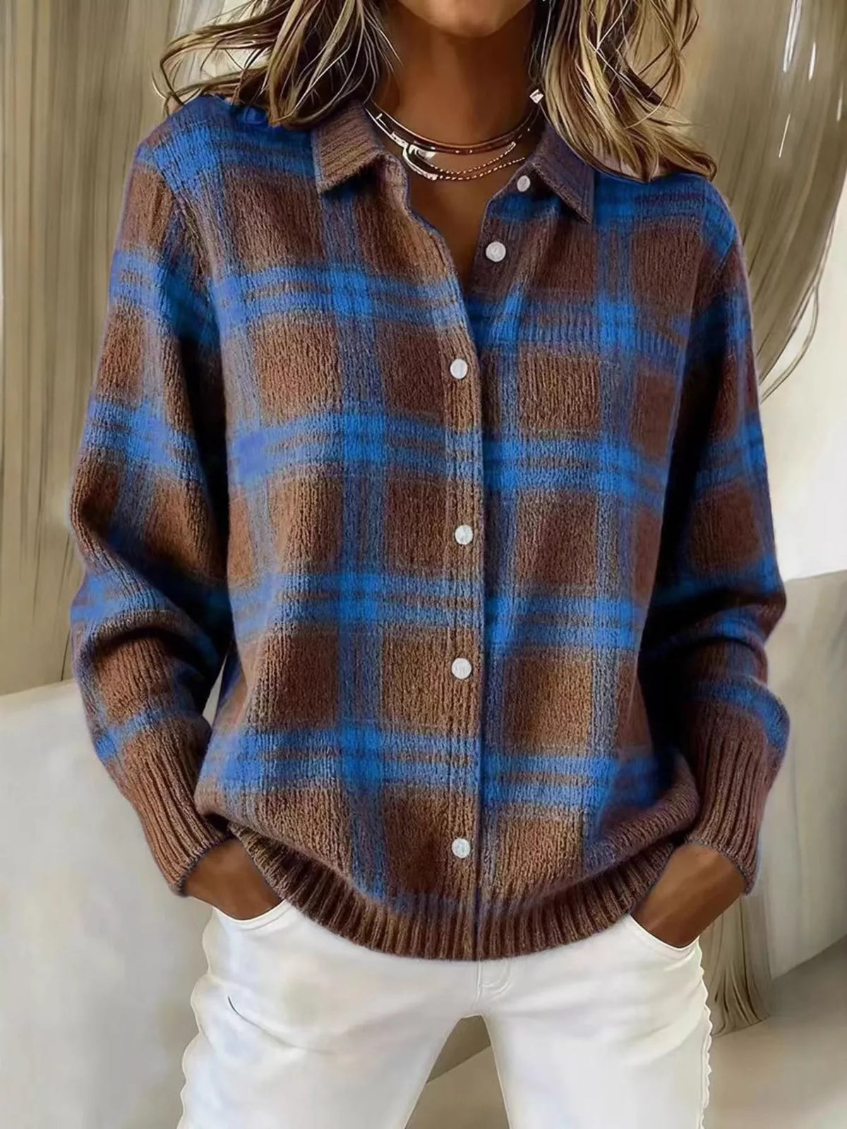 A woman wearing a brown and blue plaid button-up knit sweater with white pants, shown from the neck down in an indoor setting.