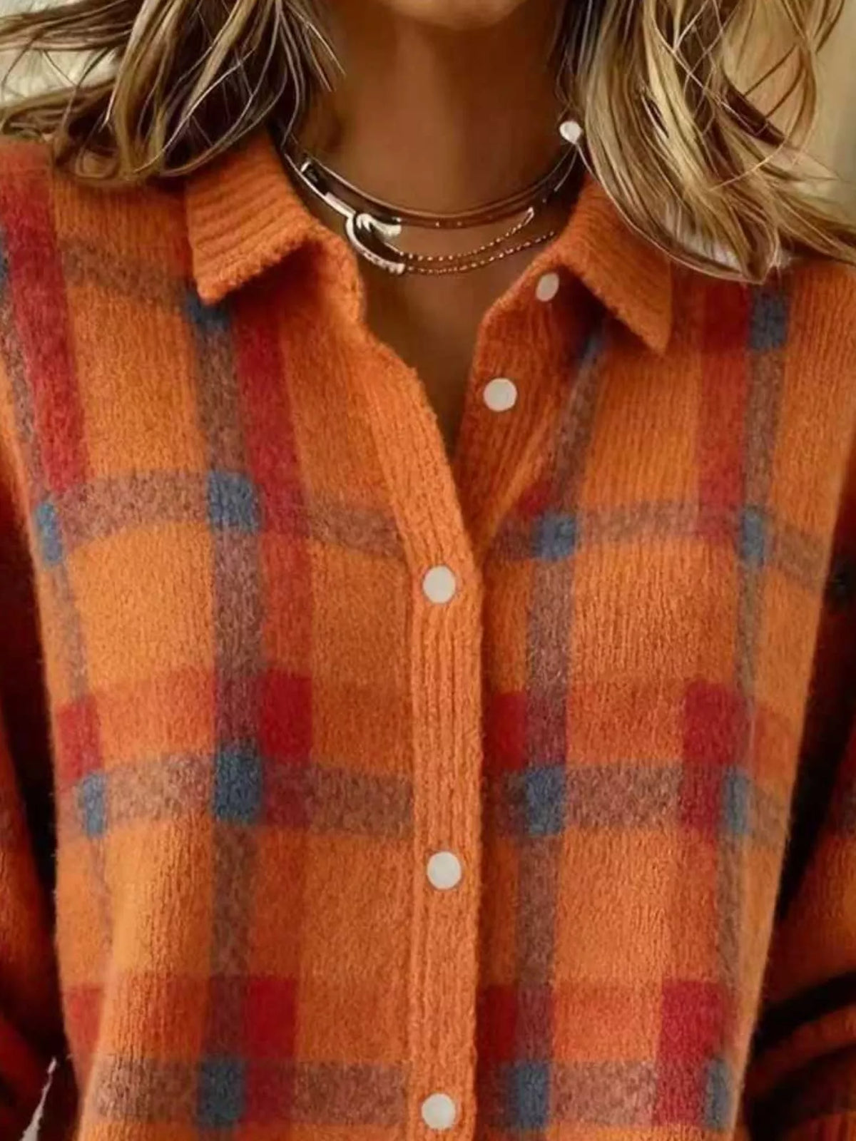 Close-up of a person wearing a fuzzy knit button-front plaid cardigan in orange with red and blue plaid stripes, layered with multiple necklaces.