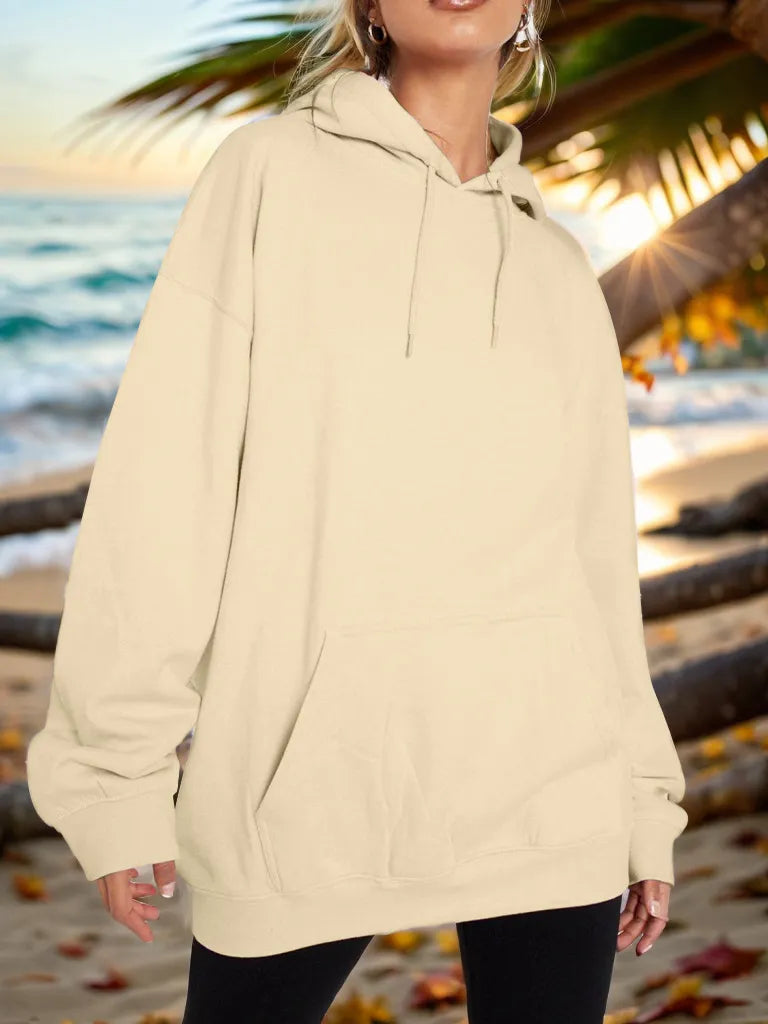 Person wearing a beige hoodie on a beach with palm trees and ocean in the background