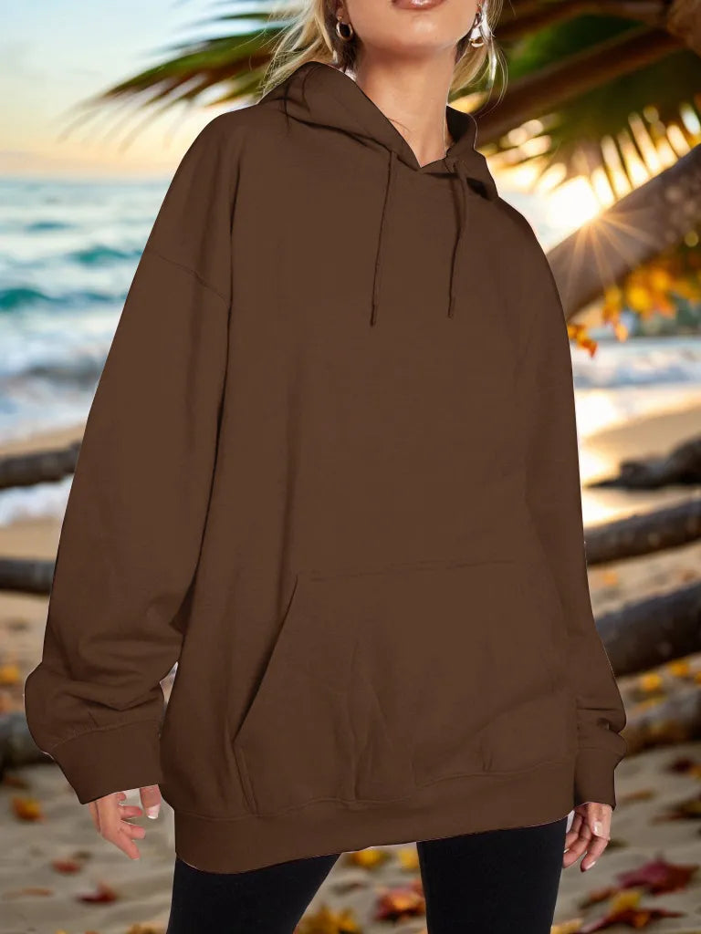 Person wearing a brown hoodie on a beach with palm trees and sunset.