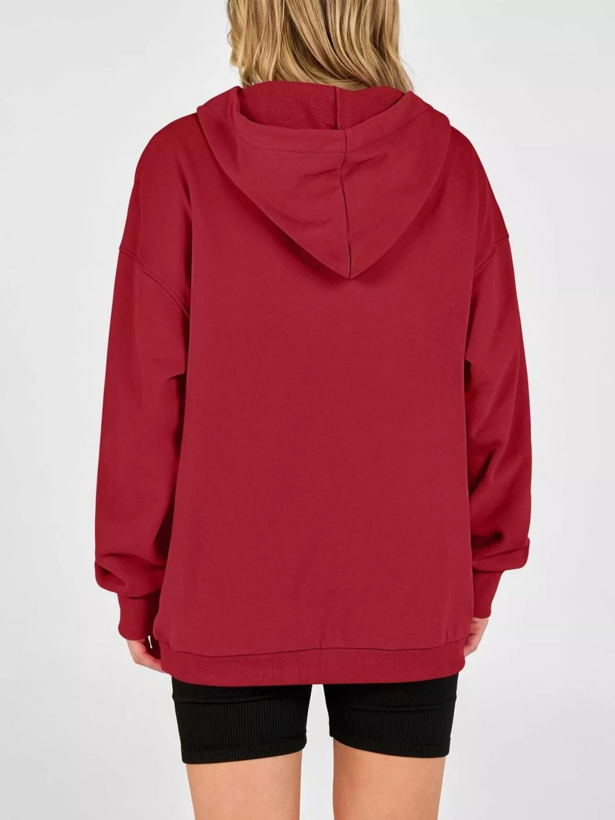 A person shown from the back wearing an oversized red hoodie with black shorts, photographed against a plain light gray studio background.