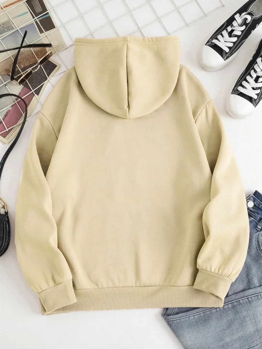 Beige hoodie on a white surface with shoes and a basket in the background