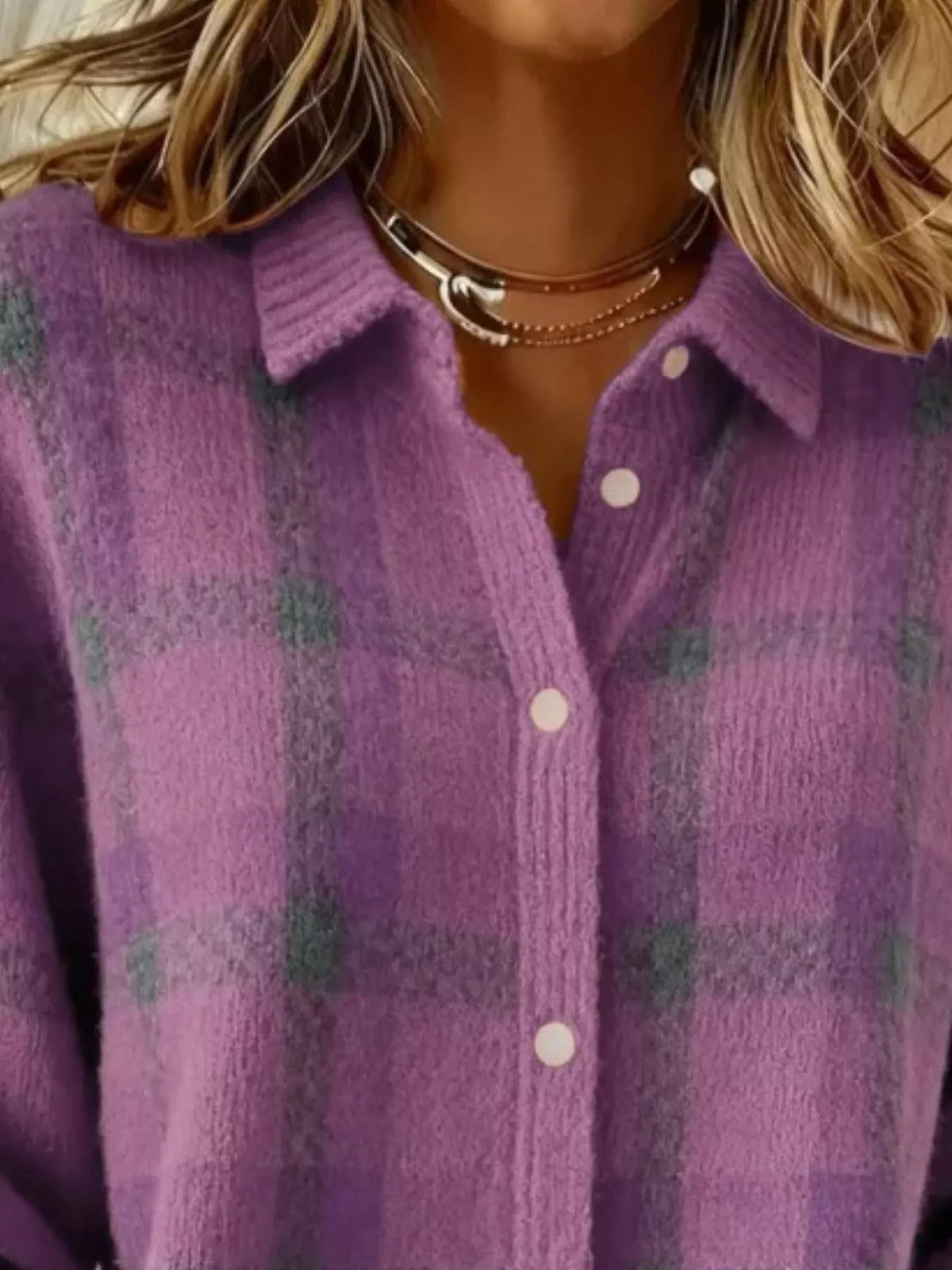 A close-up of a person wearing a fuzzy purple plaid button-up shirt with white buttons and layered gold necklaces.