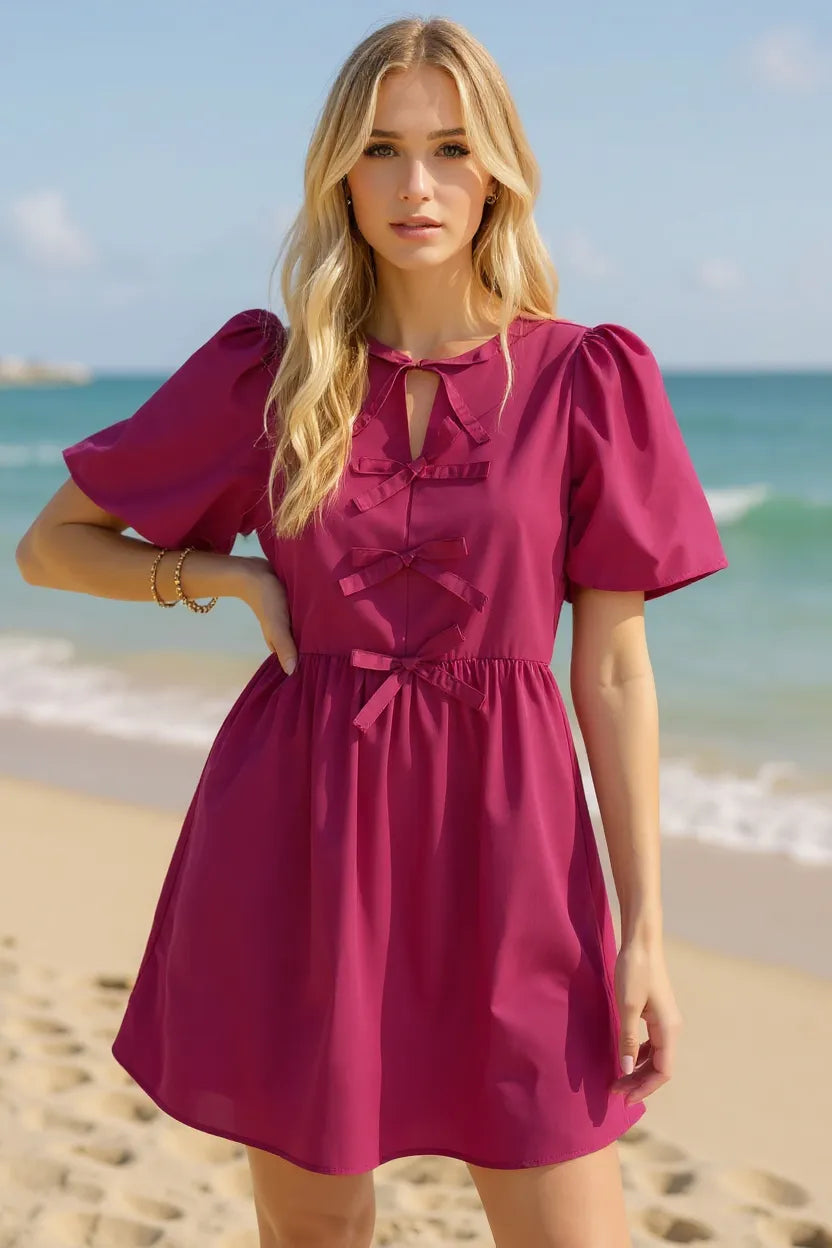 Woman in a pink dress standing on a beach with ocean in the background