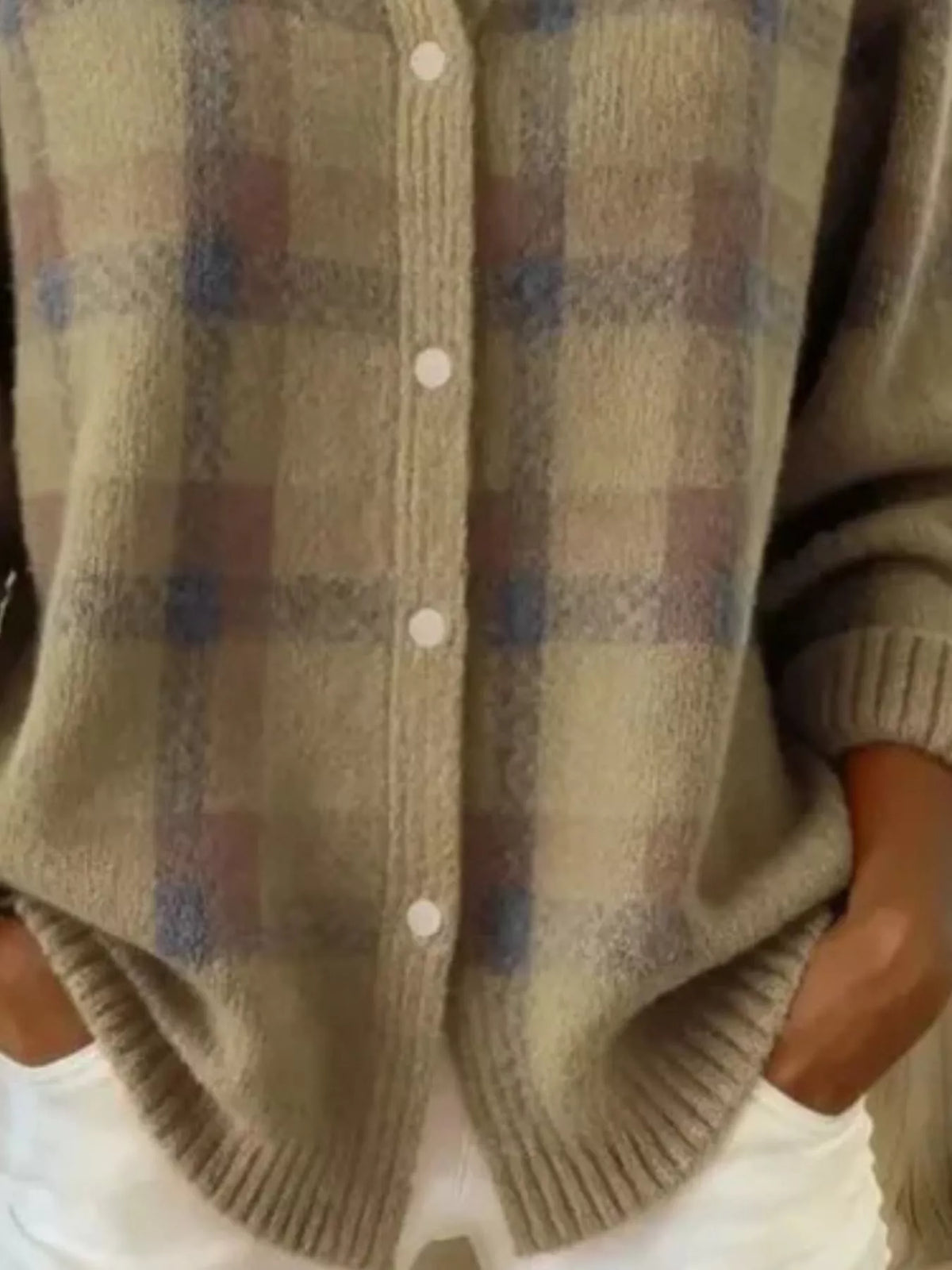 A close-up of a person wearing a fuzzy knit cardigan with a muted plaid pattern in beige, brown, and blue-gray, featuring white buttons and ribbed trim.