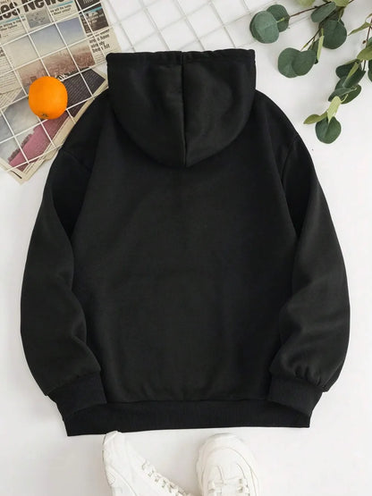 Black hoodie on a white surface with an orange and green leaves in the background