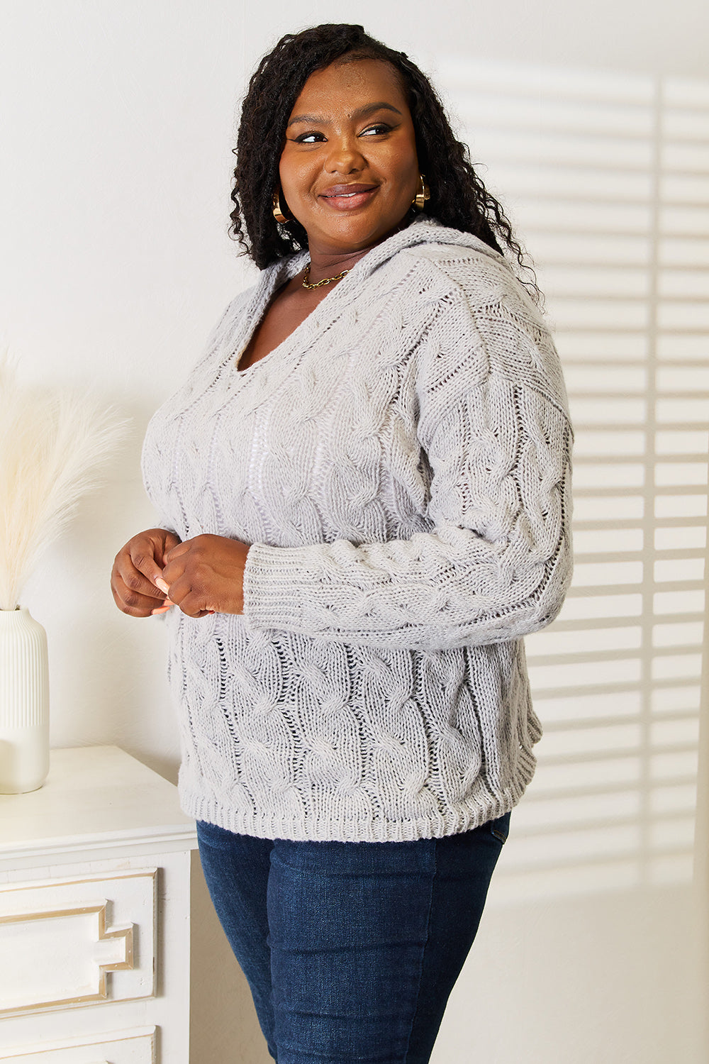 Woman wearing a gray cable knit sweater and blue jeans indoors.