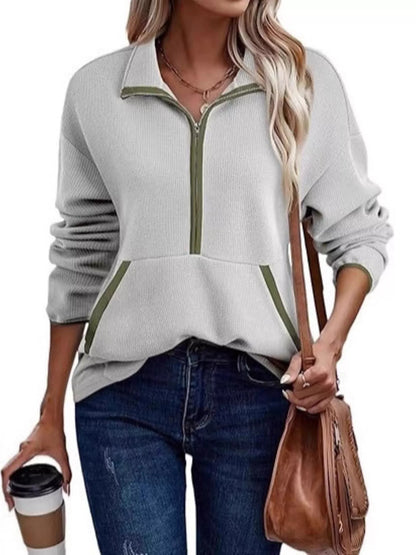 Woman wearing a light gray zip-up sweatshirt with green zipper detail, holding a brown leather bag and a coffee cup.