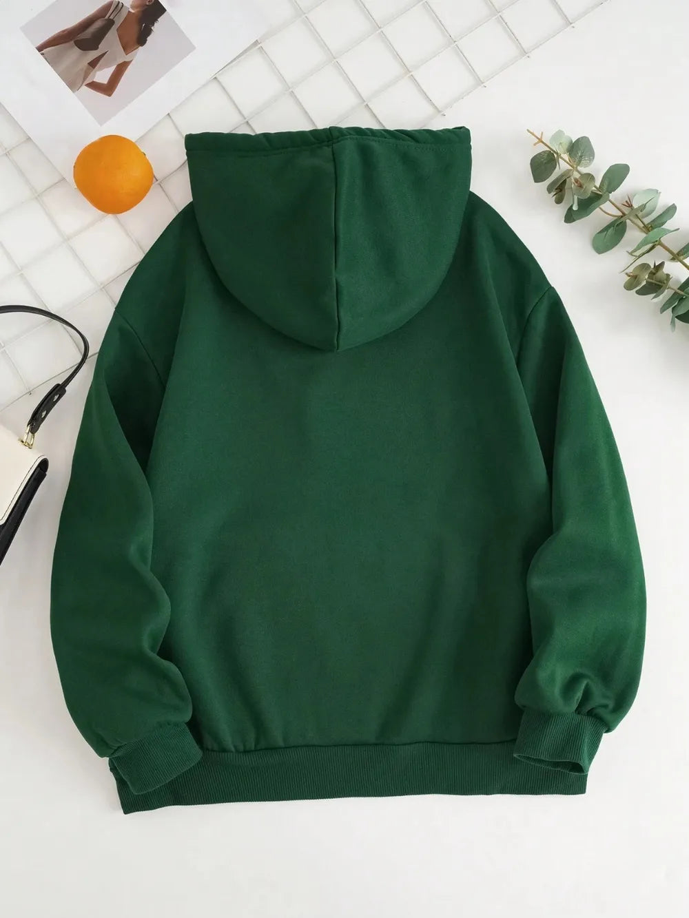 Green hoodie on a white background with a small plant and orange object.
