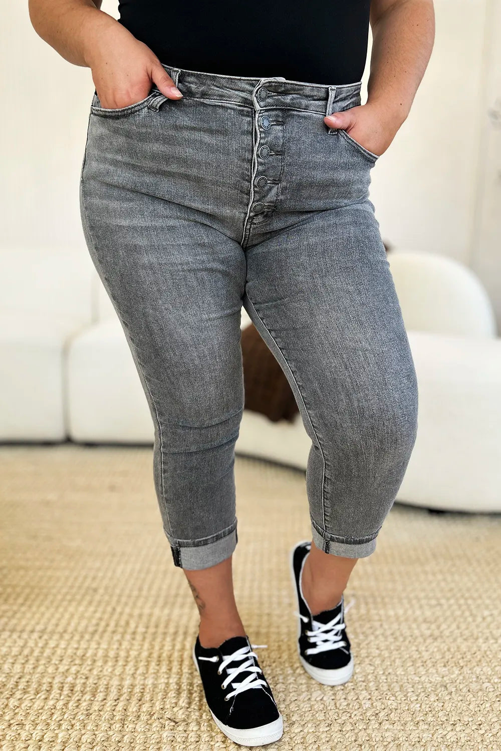 Person wearing gray jeans and black sneakers on a beige carpet.