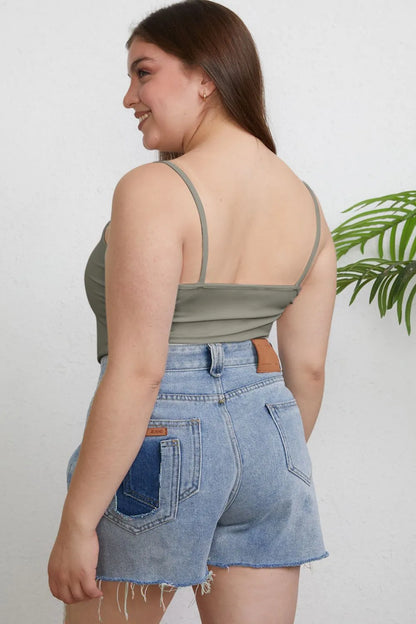 Woman wearing a green top and denim shorts against a white background