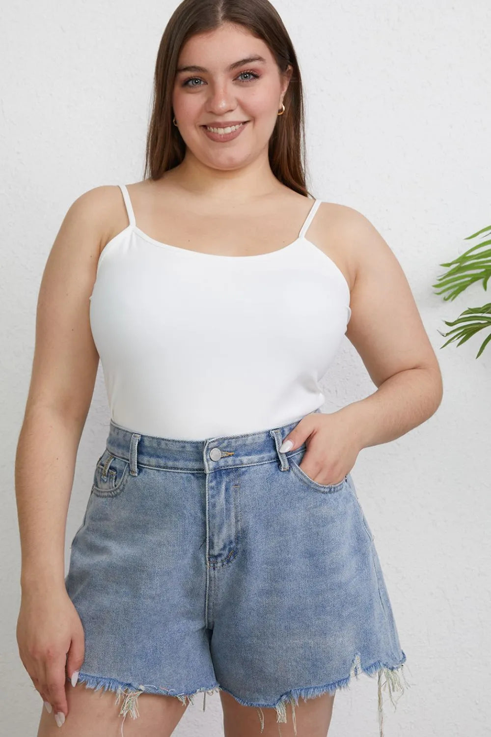 Woman wearing a white tank top and denim shorts against a plain background
