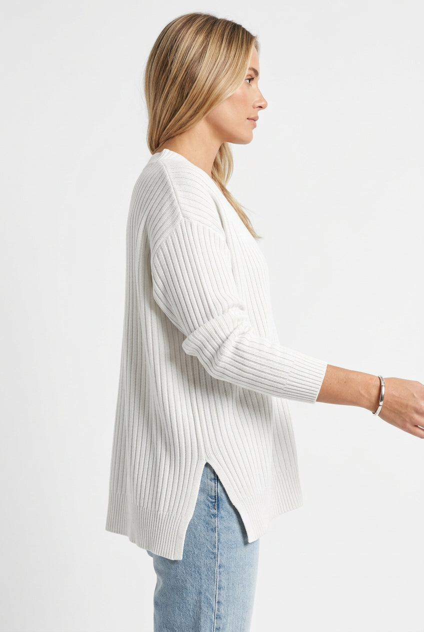 White ribbed sweater worn by a person with light blue jeans on a white background