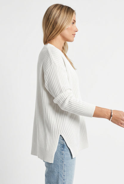 White ribbed sweater worn by a person with light blue jeans on a white background