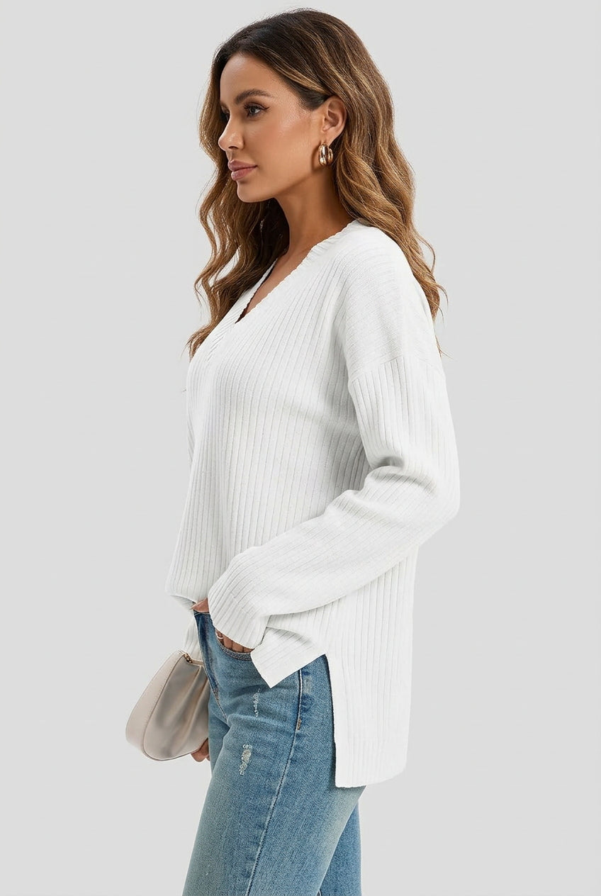 Woman wearing a white oversized ribbed knit V-neck sweater featuring long sleeves, side-slit hem, relaxed fit silhouette, and soft textured fabric for cozy everyday styling. Color & Features and Specs