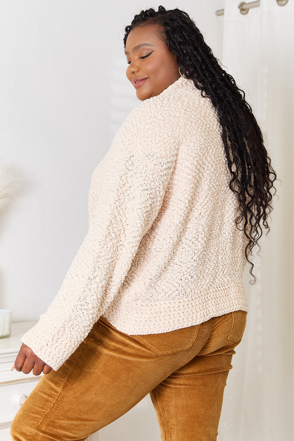 Woman wearing a beige sherpa jacket and brown pants in a neutral setting