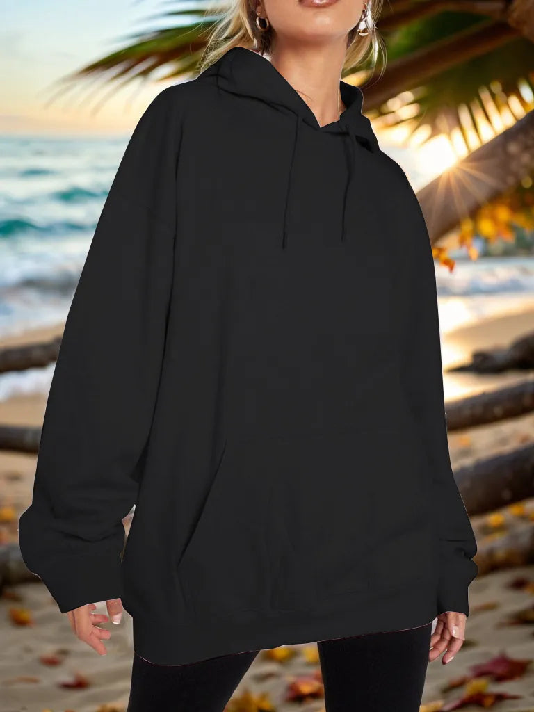 Person wearing a black hoodie on a beach with palm trees and sunset.