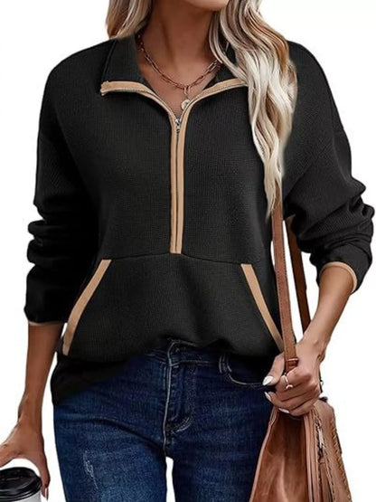 Black zip-up sweatshirt with beige accents worn by a person, holding a brown bag.