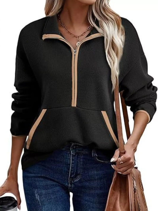 Black zip-up sweatshirt with beige accents worn by a person, holding a brown bag.