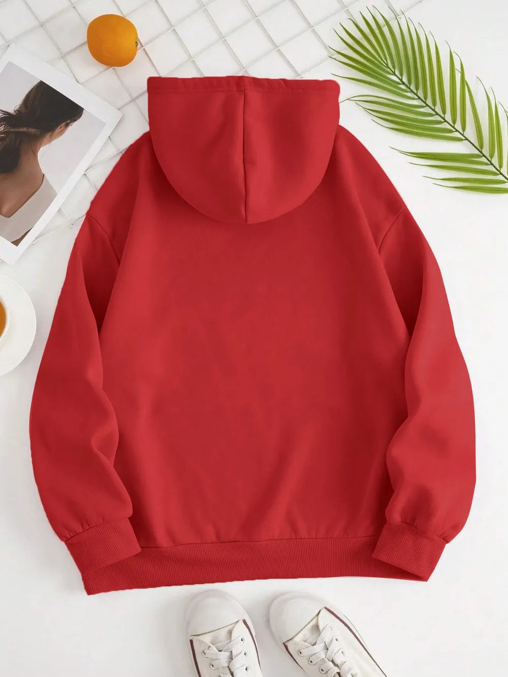 Red hoodie on a white background with green leaves and a person partially visible.