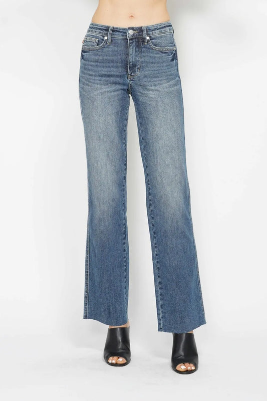 A model from the waist down wearing medium-wash blue denim jeans with a straight-to-flare leg and black open-toe heeled sandals, photographed against a plain white studio background.