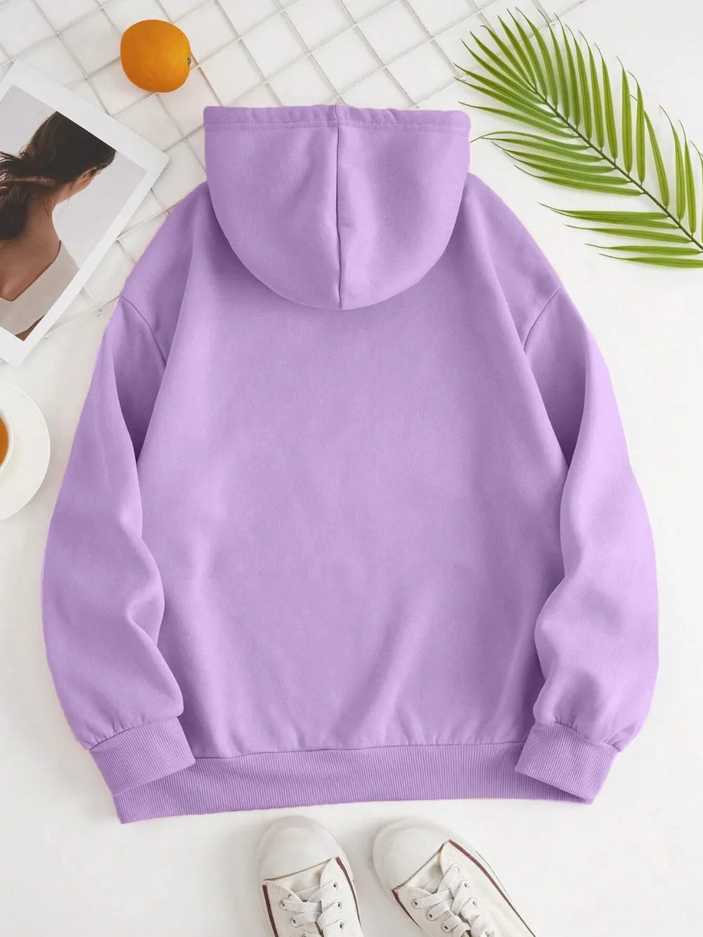 Purple hoodie on a white surface with a person and green leaves in the background