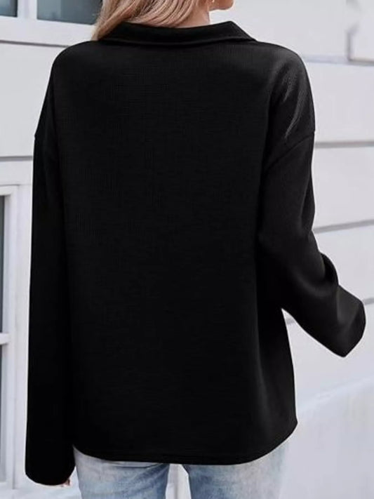 Black long-sleeve top worn by a person with a blurred background