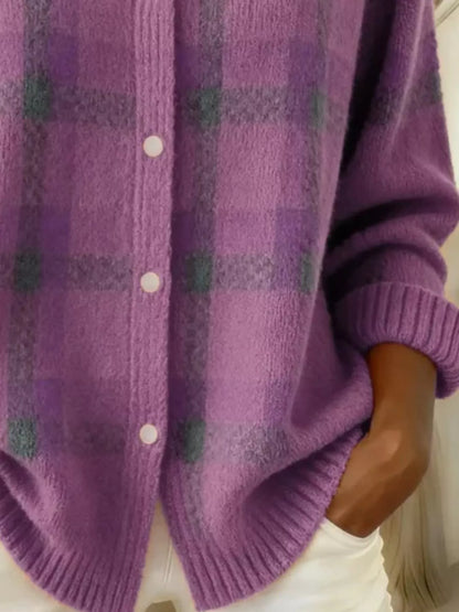 A close-up of a person wearing a fuzzy purple knit cardigan with a subtle plaid pattern in darker purple and muted green, featuring white buttons and ribbed cuffs.