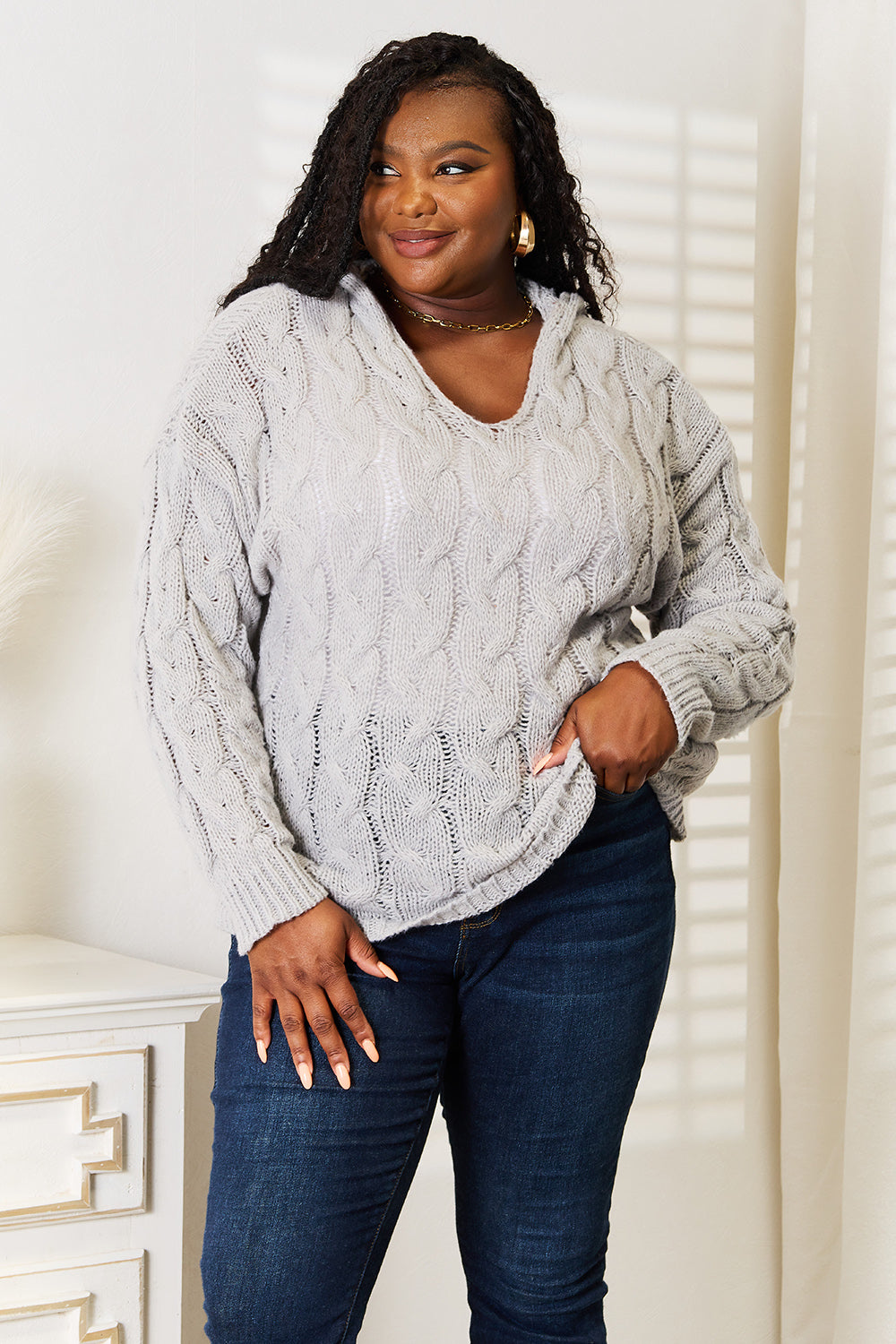 Woman wearing a gray cable knit sweater and dark blue jeans indoors.