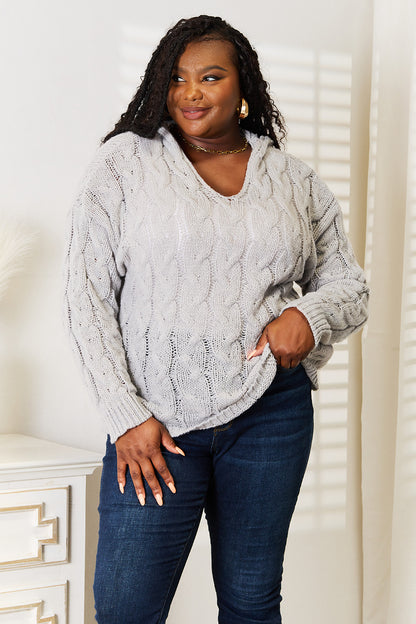 Woman wearing a gray cable knit sweater and dark blue jeans indoors.