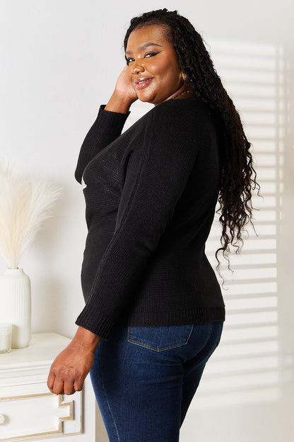Woman wearing a black cardigan and blue jeans standing indoors.