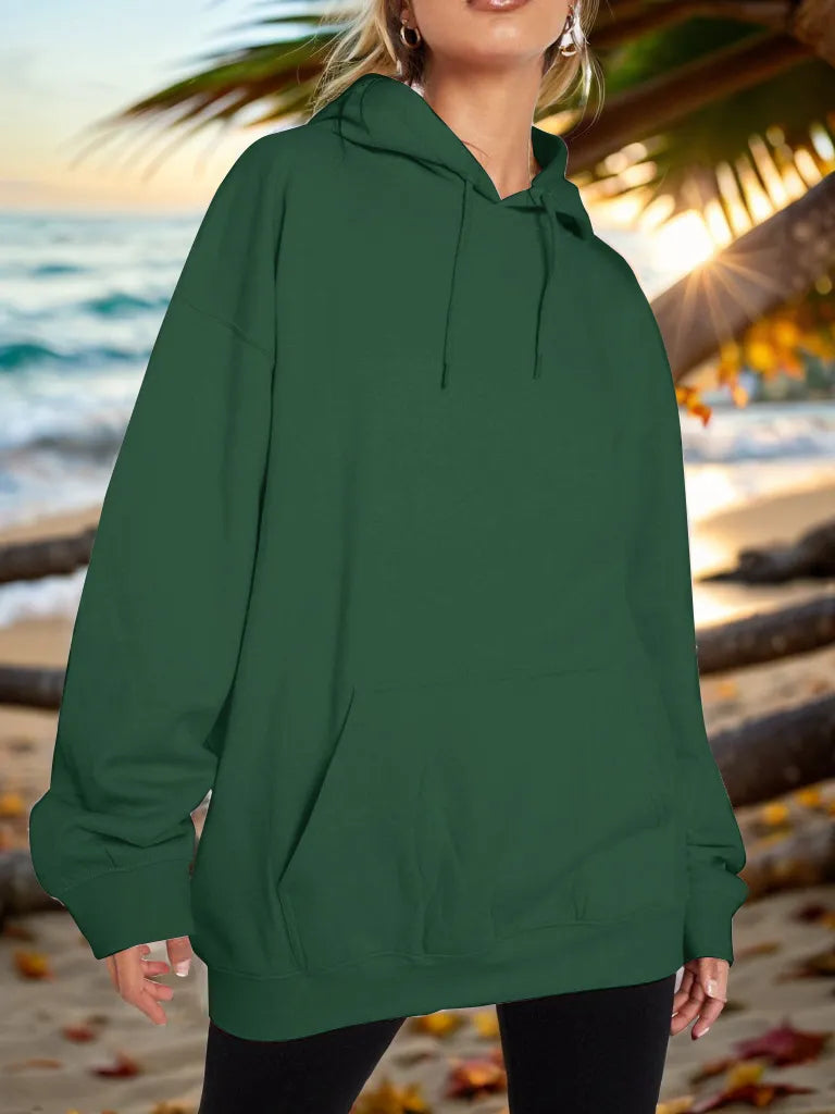 Person wearing a green hoodie on a beach with palm trees and ocean in the background
