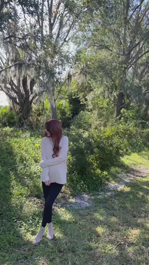 Woman wearing a white oversized ribbed knit V-neck sweater featuring long sleeves, side-slit hem, relaxed fit silhouette, and soft textured fabric for cozy everyday styling.Video 